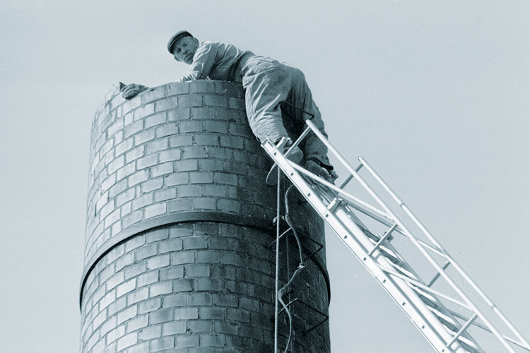 A man standing on a ladder at the top of a chimney A man standing on a ladder at the top of a chimney