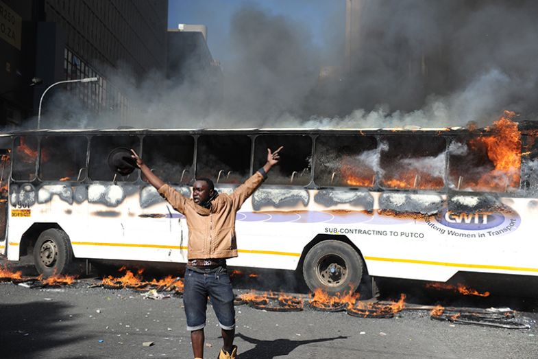 A Wits University student throws stones while a bus burns during the #FeesMustFall protests on 10 October 2016 in Johannesburg, South Africa.