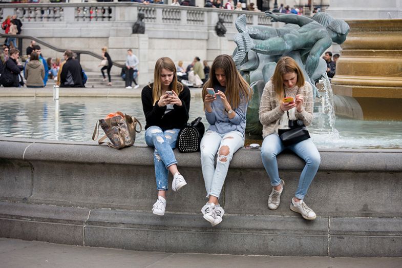 Three young women sit on fountain in Trafalgar Square looking at phones Three young women sit on fountain in Trafalgar Square looking at phones