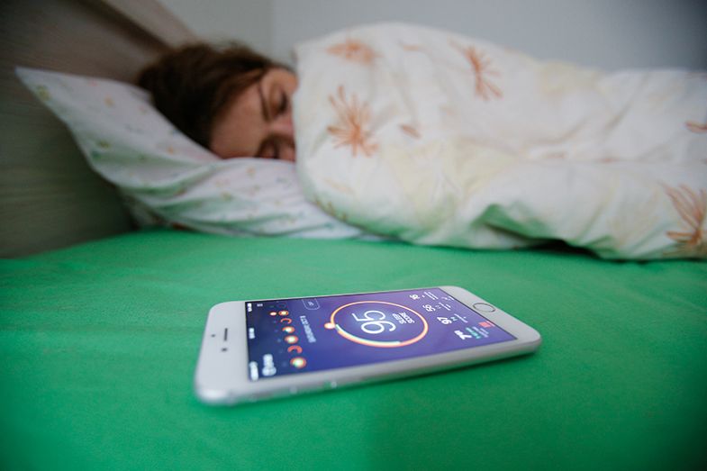 A woman sleeps, with a health app on her phone in the foreground A woman sleeps, with a health app on her phone in the foreground