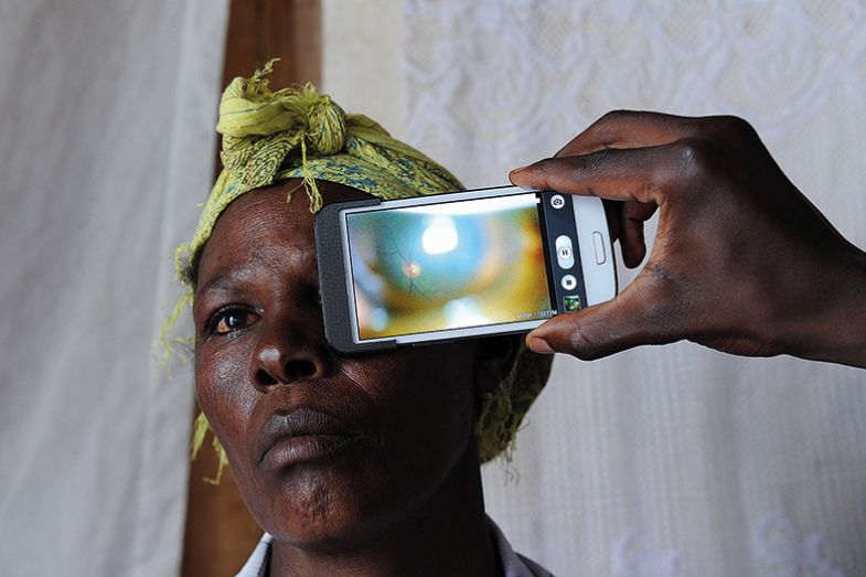 A technician in Kenya scans the eye of a woman with a phone app (used to scan people's eyes and optic nerves, to detect eye diseases, including cataracts and glaucoma). A technician in Kenya scans the eye of a woman with a phone app (used to scan people's eyes and optic nerves, to detect eye diseases, including cataracts and glaucoma).