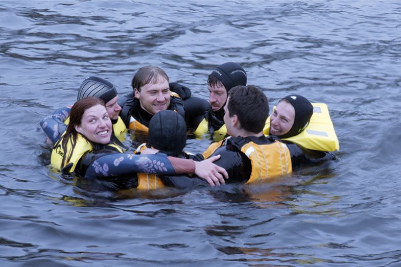 A group of people in wet suits and life preservers in the water A group of people in wet suits and life preservers in the water