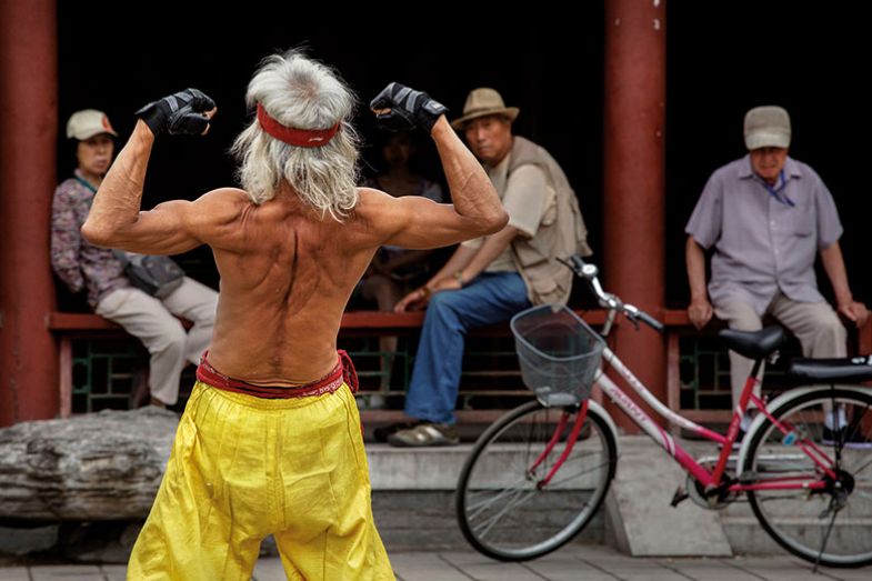 elderly Chinese man flexes his muscles as he performs a martial arts routine on the street, Beijing, China elderly Chinese man flexes his muscles as he performs a martial arts routine on the street, Beijing, China