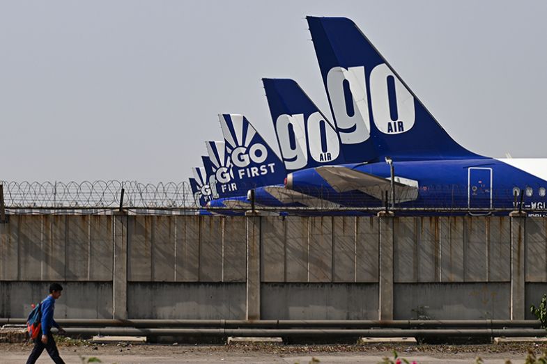 A man walks on a road past Go First aircrafts, that are parked at the tarmac at the airport in New Delhi, India, 2023. To illustrate Asian students deciding on where to study.