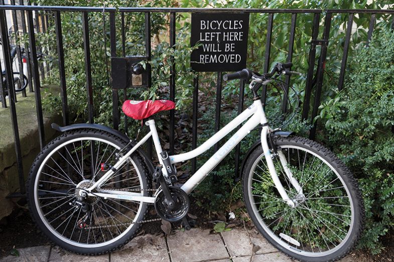 Bicycle parked and locked underneath a Bicycles left here will be removed sign. Bicycle parked and locked underneath a Bicycles left here will be removed sign.