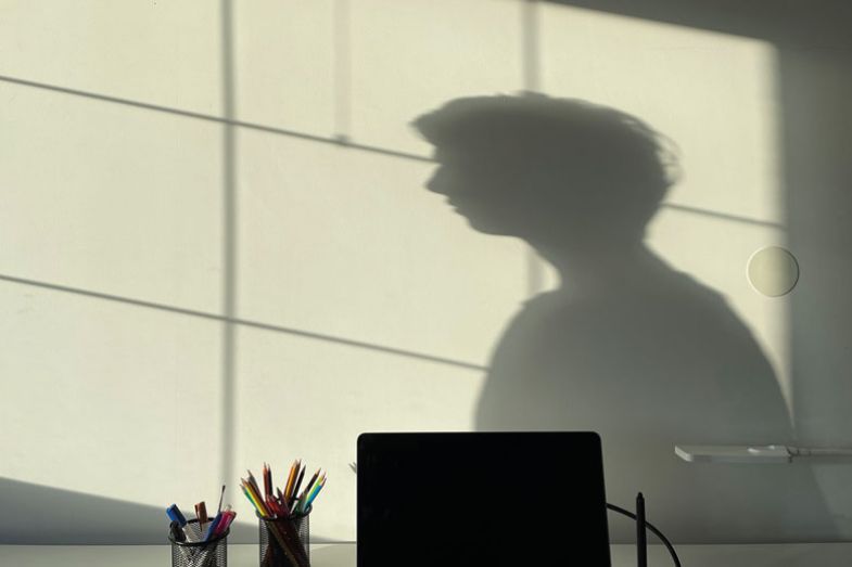 Person shadow on wall Person shadow on wall desk with laptop and stationary in front as a metaphor for Many students are distressed and quarantined, unsure how to finish, how to see people, how to live normally