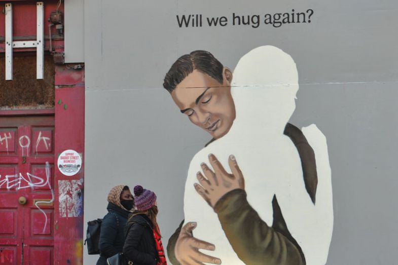 people walking past A mural 'Will we hug again?' people walking past A mural 'Will we hug again?'