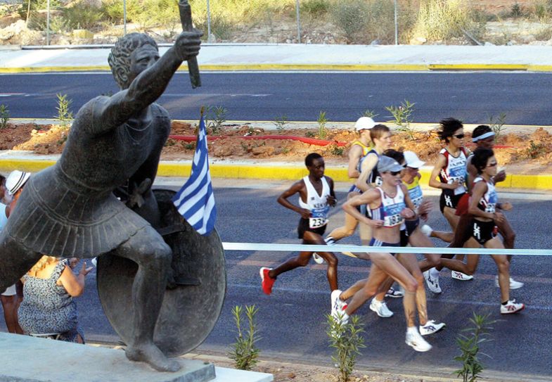   Japan's Mizuki Noguchi (front) leads the pack along with Britain's Paula Radcliffe (C, wearing cap no1831) as they run past a statue depicting a ancient Greek runner during the Olympic Games women's Marathon race in Athens
