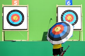  An archer holding an umbrella with a target design checks the target during the first day of an archery test event. To illustrate challenging new UKRI targets for industry-funded research.