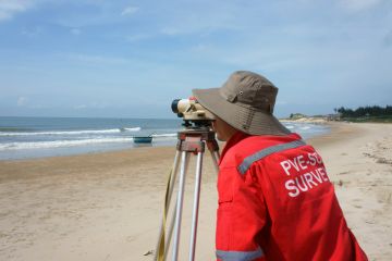 Binh Thuan, Viet Nam - October 21, 2014 Asian engineer work on Vietnamese beach, man looking in theodolite to survey sea level, measurement device set on tripod, Vietnam, Oct 21, 2013