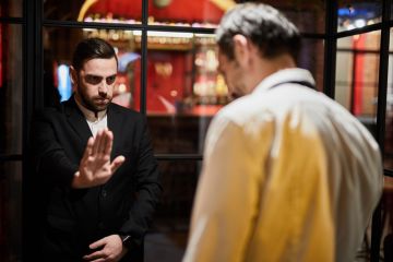 A security guard blocks a doorway, symbolising university access