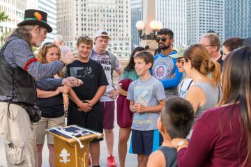 Chicago, IL, August 17, 2017 Downtown Chicago, a street performer magician entertains tourist families. Chicago attracts millions of visitors each year.