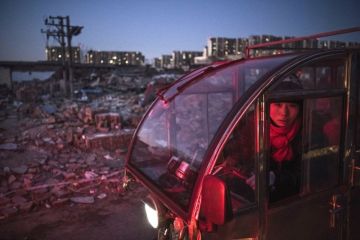 A Chinese woman drives past collapsed buildings
