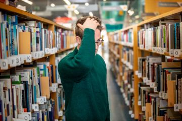 A man looks confused in a library aisle A man looks confused in a library aisle