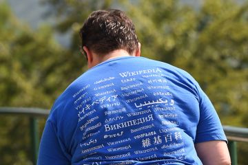 A man attending the Wikimania meeting, wears a shirt reading "Wikipedia" in different languages.