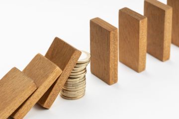 A pile of coins stops a row of dominoes from falling, symbolising capital investment