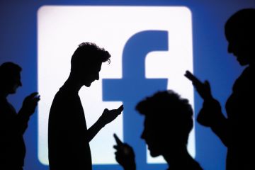 Silhouettes of people using smartphones in front of Facebook logo Silhouettes of people using smartphones in front of Facebook logo