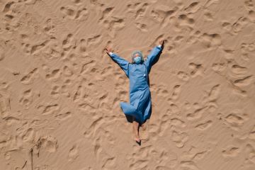 female doctor in medical gear lying on sandy beach