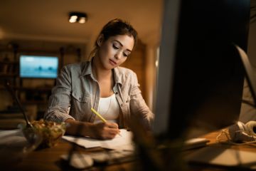 Female student taking notes while learning at night at home