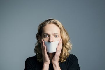 A man holds paper in front of his mouth, symbolising non-disclosure agreements