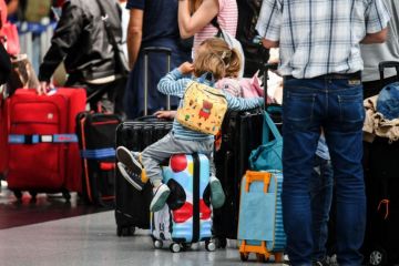 Travellers sit on their suitcases at the check-in counters Travellers sit on their suitcases at the check-in counters