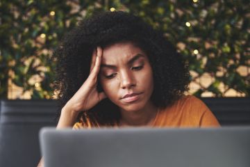 A sad young woman looks at a laptop
