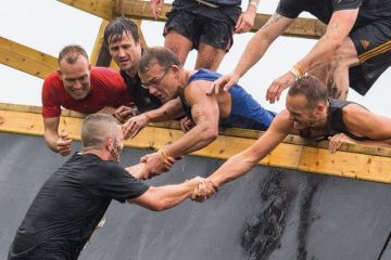Group of men assisting teammate on obstacle course Group of men assisting teammate on obstacle course