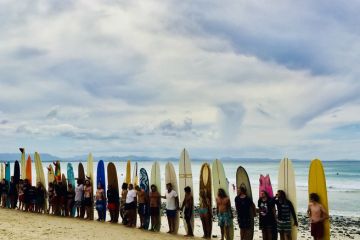 horizontal seascape of surfers with surfboards on sand at surf competition on overcast day at famous place Wategos Beach Byron Bay Australia