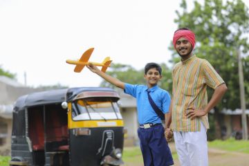 A young Indian rikshaw driver and his little brother holding a toy plane, symbolising international education