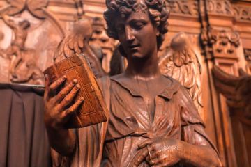 Reading angel holding an old book, wooden statue in 17th century catholic church Saint Charles Borromeo on March 31, 2018.