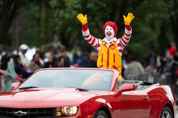 Ronald McDonald waving at spectators while going on a camaro down the road