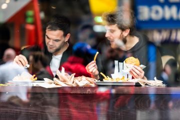 Two men guy friends sitting in fast food cafe looking outside window counter