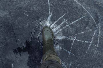 Fisherman foot on broken cracked thin ice at lake Fisherman foot on broken cracked thin ice at lake