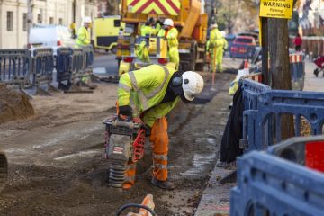 Man in yellow vest drilling the pavement in a London Street.