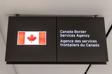 A Canadian flag next to a bilingual sign reading Canada Border Services Agency located in Terminal 3 of Toronto Pearson airport