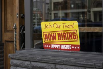 Now hiring sign is seen at the storefront of a local business