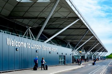 Passengers with luggage walking towards the entrance of London Stansted Airport 