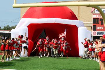 High school football team entering the field through a blow up football helmet tunnel with cheerleaders in a line cheering. High school football team entering the field through a blow up football helmet tunnel with cheerleaders in a line cheering.