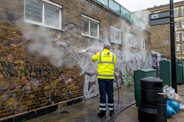 A Tower Hamlet Council worker cleaning graffiti off a building with a jet power wash. A Tower Hamlet Council worker cleaning graffiti off a building with a jet power wash.