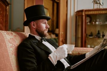 Man wearing formal suit and top hat sitting on sofa reading newspaper Man wearing formal suit and top hat sitting on sofa reading newspaper