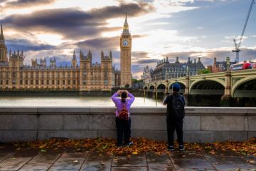 Rear view of a tourist couple taking photos of Big Ben and the Houses of Parliament from the south side of Westminster Bridge on the Thames embankment. Rear view of a tourist couple taking photos of Big Ben and the Houses of Parliament from the south side of Westminster Bridge on the Thames embankment.