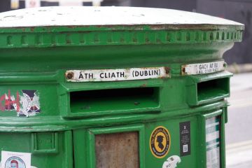 A close-up of a traditional green Irish post box in Dublin, with its distinctive Gaelic and English text A close-up of a traditional green Irish post box in Dublin, with its distinctive Gaelic and English text