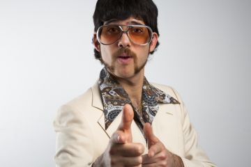 A man pulls a cheesy pose in 1970s clothing. Academics need to strike the right tone with their academic profiles if they want to attract PhD students.