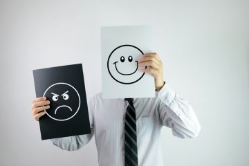 Man holding smiling and frowning faces Man holding smiling and frowning faces