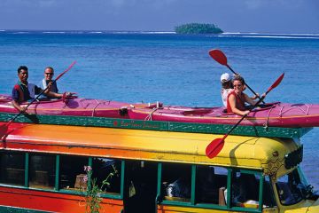 people sitting in kayaks on top of a bus