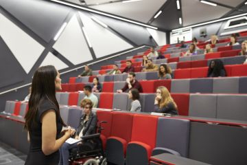 A woman lectures to a half-empty lecture theatre