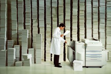 Man in white coat photocopying, illustrating the burden of administrative tasks in academia. Man in white coat photocopying, illustrating the burden of administrative tasks in academia.