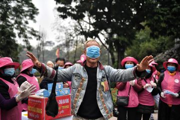 Man with medical mask over eyes surrounded by a crowd of people