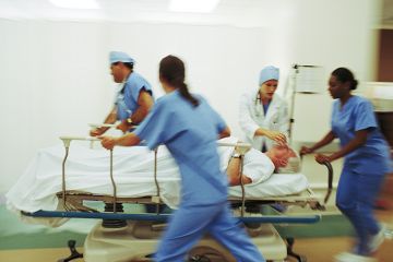 Four medics pushing mature male patient through hospital corridor on trolley. Four medics pushing mature male patient through hospital corridor on trolley.