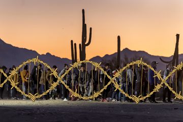 Immigrants line up at a remote U.S. Border Patrol processing centre after crossing the U.S.-Mexico border in Lukeville, Arizona. With added barbed wire twisted in the shape of a DNA helix. To illustrate Donald Trump's divisive misuse of genetics.
